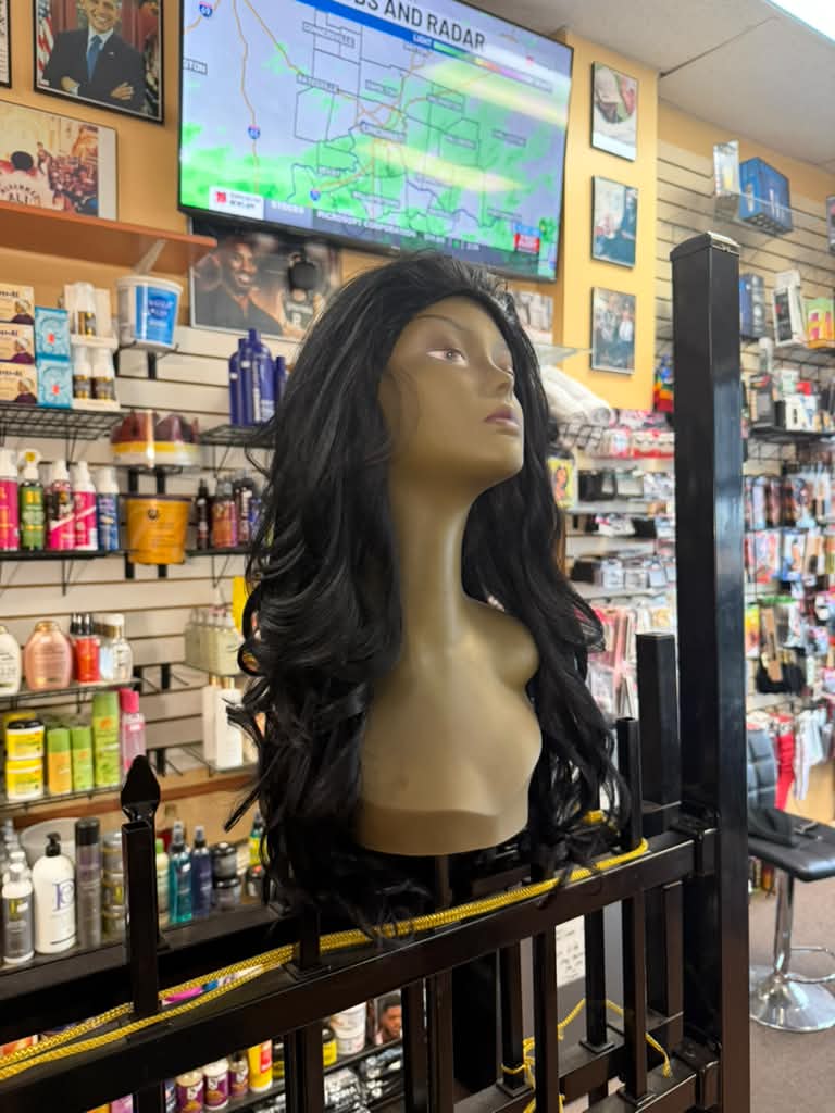 Side view of a long black layered wavy wig on a mannequin in the wig department at Beyond Image Suites and Supplies